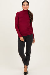 woman wearing a maroon long sleeve turtleneck top and black flared jeans