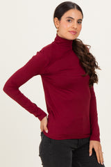 woman wearing a burgundy long sleeve turtleneck top and black jeans, posing with one hand on her hip
