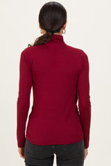 woman wearing a burgundy long sleeve turtleneck top seen from the back with a sleek fit and minimal styling