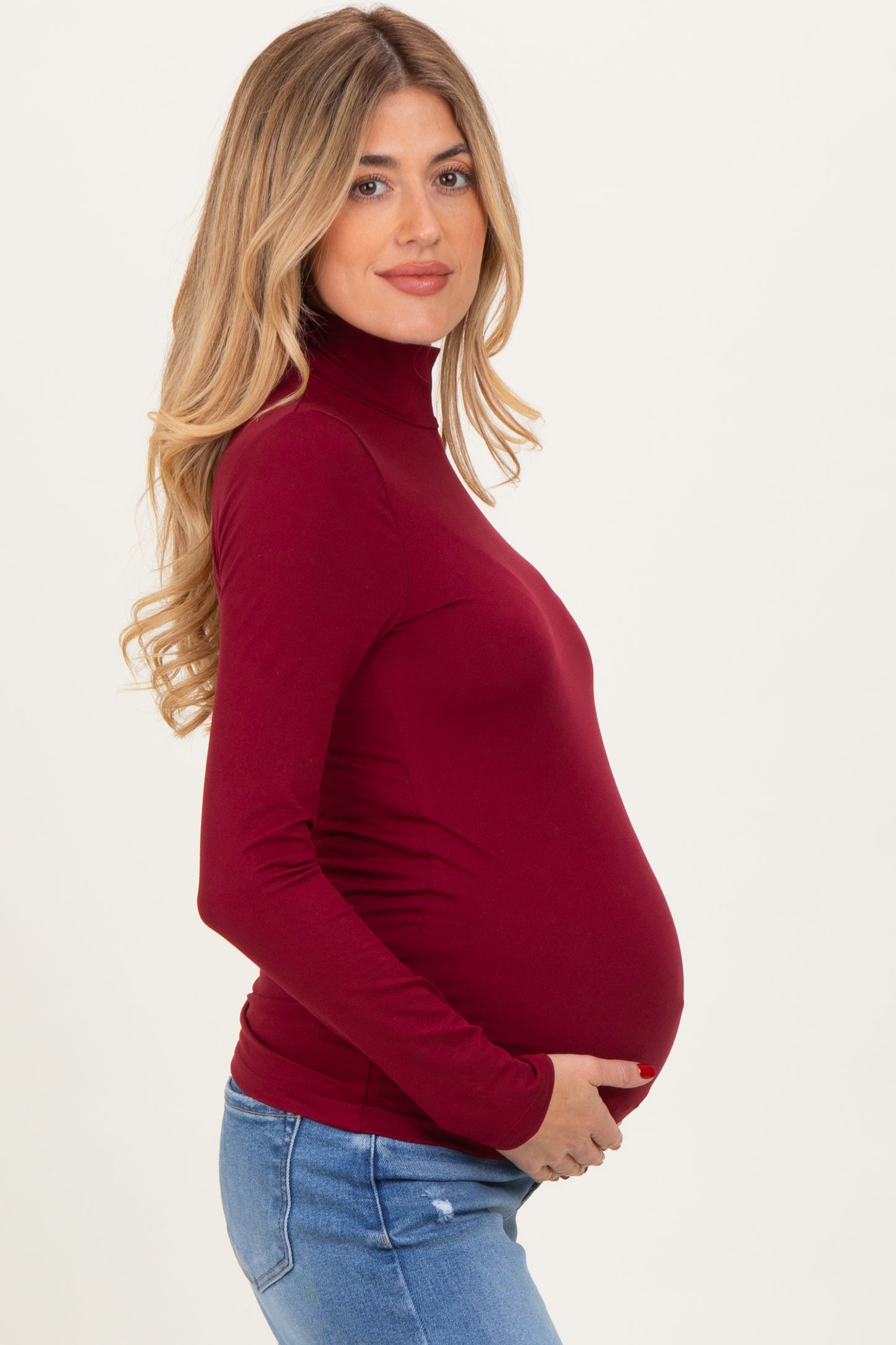 woman wearing a burgundy long sleeve maternity top and holding her baby bump