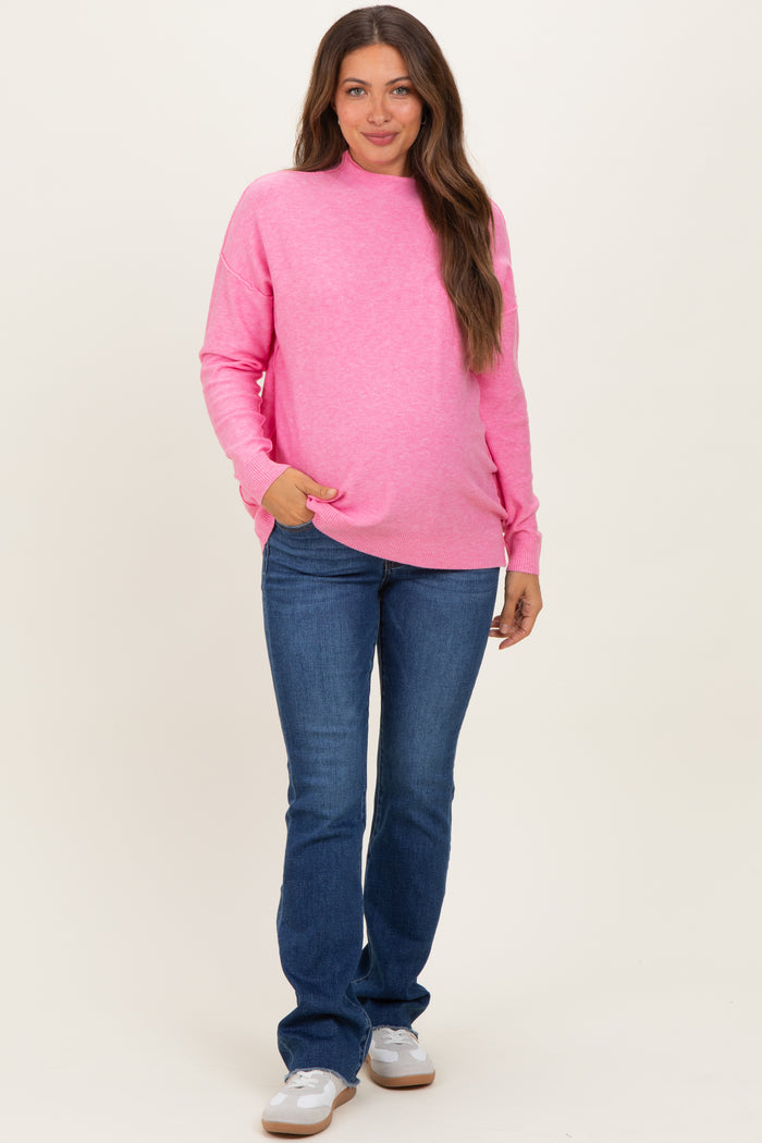 woman wearing a bright pink maternity sweatshirt and blue jeans, showcasing her baby bump
