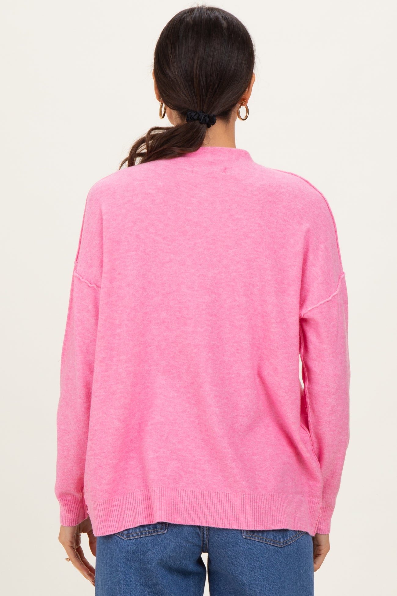 woman wearing a pink oversized sweater with a round neckline and dropped shoulders, viewed from the back