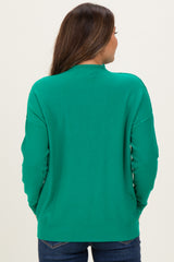 woman wearing a green maternity sweater, showing a relaxed fit and back details, with blue jeans