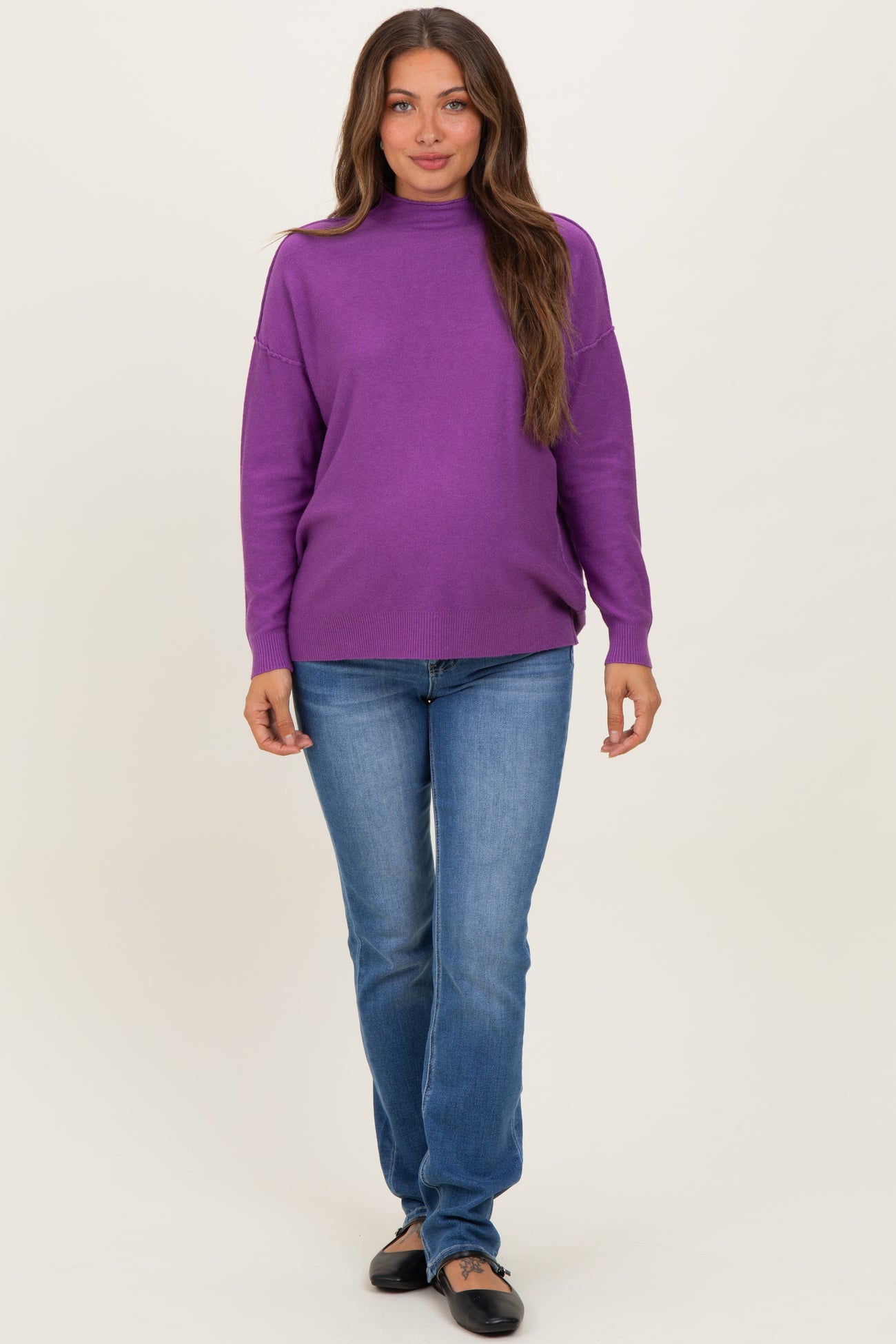woman wearing a purple maternity sweater and blue jeans, with a visible baby bump