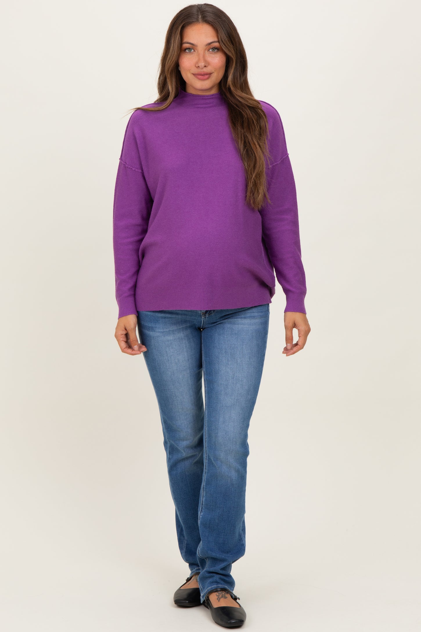 woman wearing a purple maternity sweater and blue jeans, with a visible baby bump