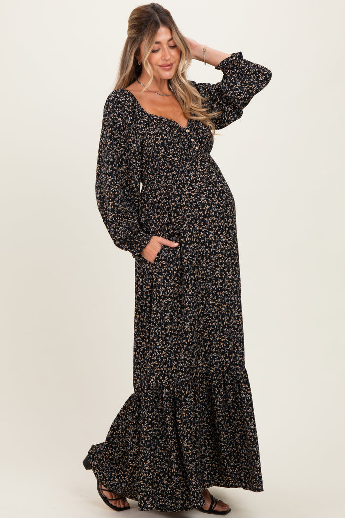 woman wearing a black floral maternity maxi dress with long sleeves and pockets, showing her baby bump