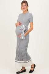 woman wearing a grey ribbed maternity dress with a tie waist and white pleated hem, showing her baby bump