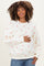 woman wearing a cream maternity sweatshirt with red heart prints and holding her baby bump
