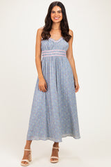woman wearing a light blue floral maxi dress with a smocked bodice and braided detail, standing on a neutral background