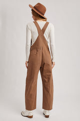 woman wearing a cream long sleeve top and brown denim overalls with wide legs and a brown hat