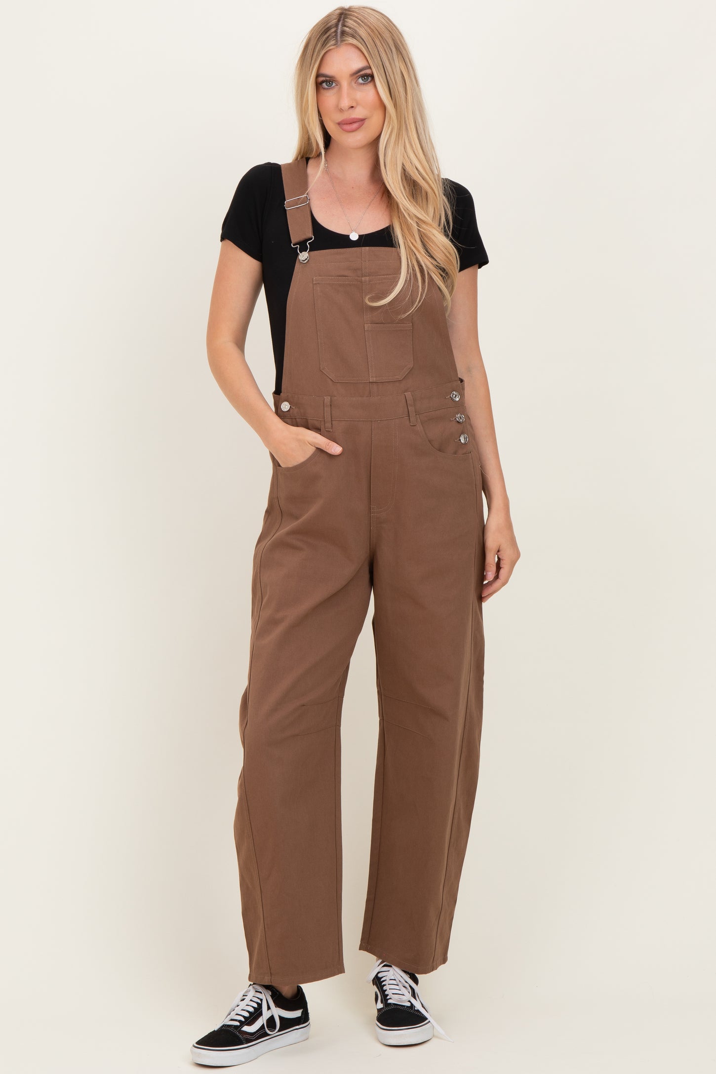 woman wearing a black t-shirt and brown overalls with wide legs and side buttons