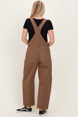 woman wearing brown overalls with a black t-shirt, showing the back view with adjustable straps and loose fit