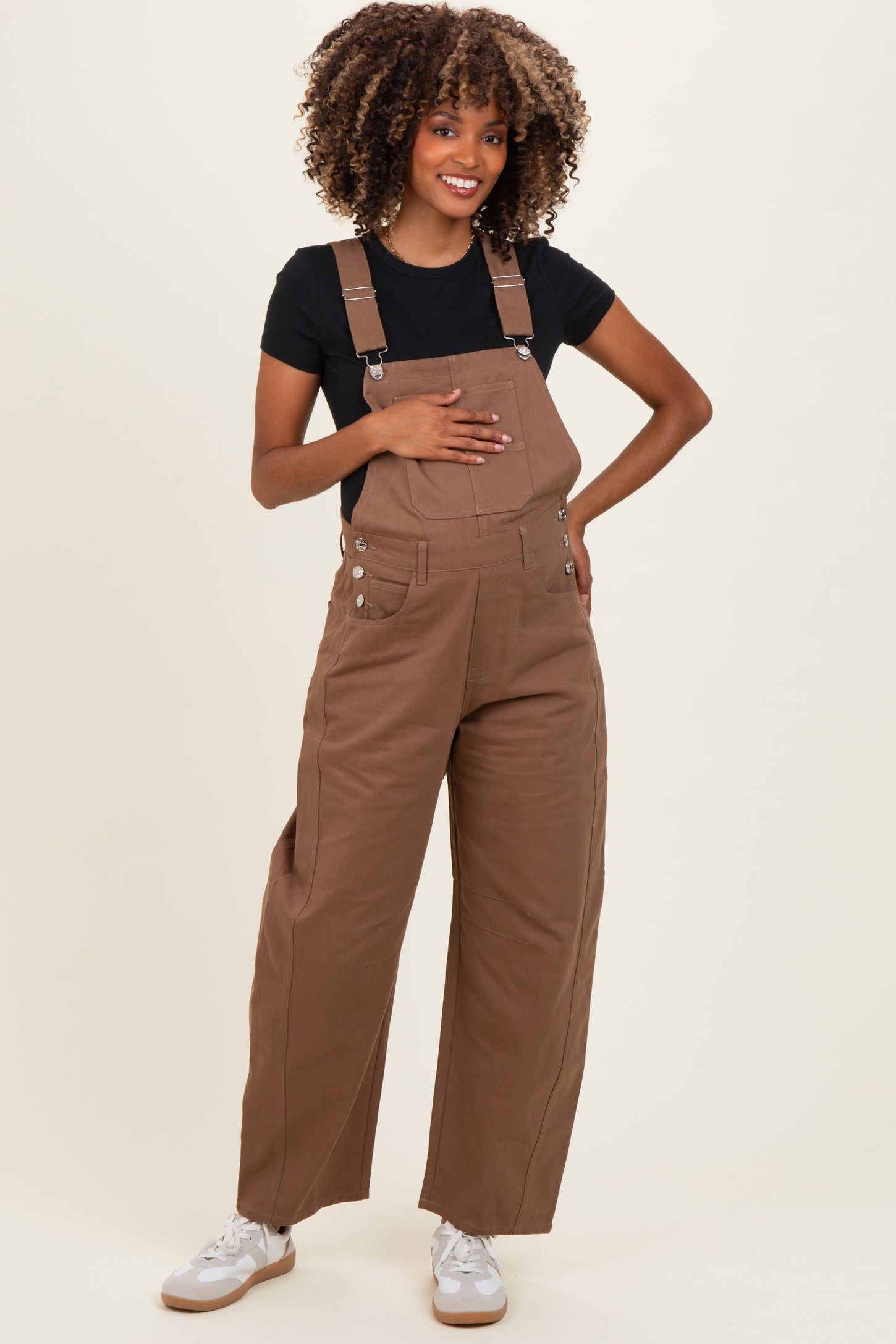 woman wearing a brown maternity overall with a black t-shirt and holding her baby bump