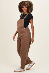 woman wearing light brown maternity overalls with a black t-shirt and sneakers, showing a baby bump