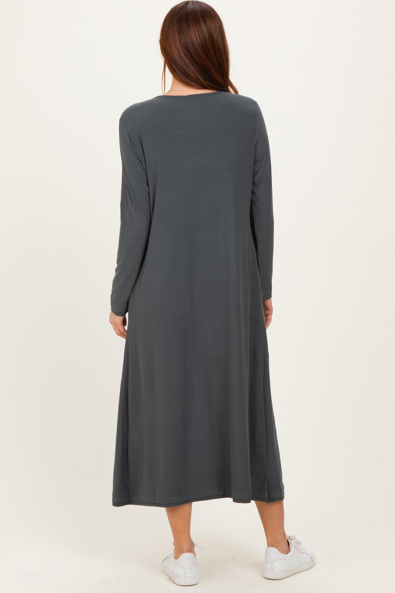 woman wearing a long sleeve dark gray maxi dress, standing with her back to the camera