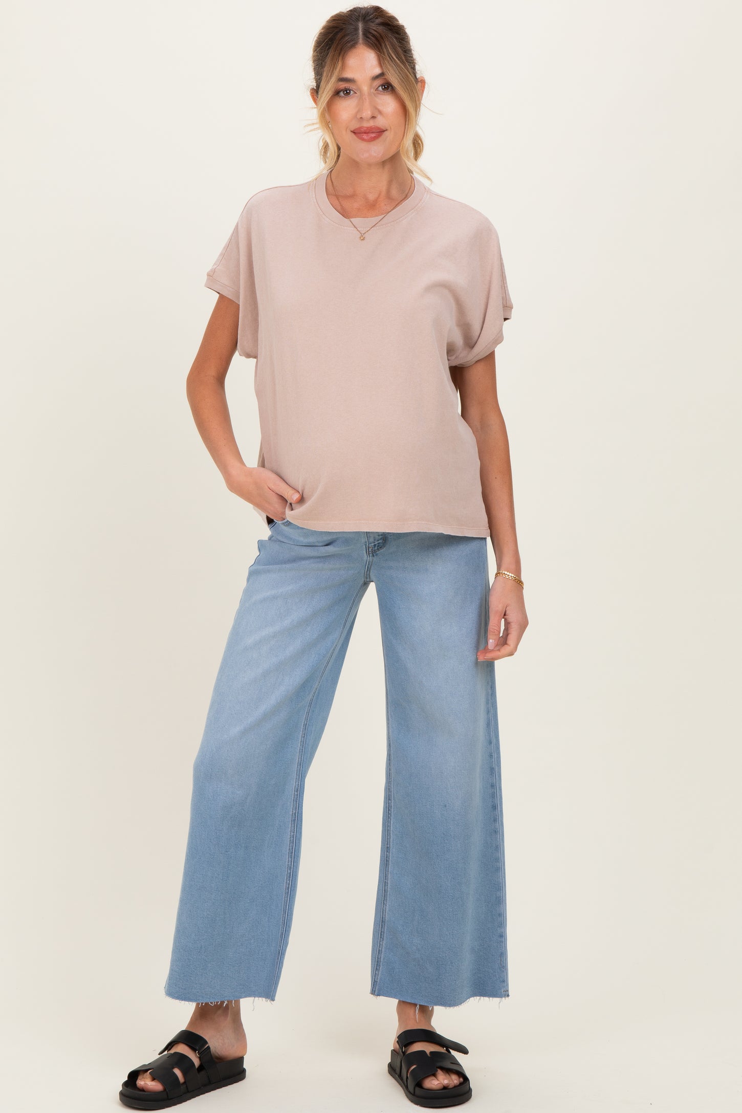 woman wearing a blush pink maternity top and high-waisted wide-leg jeans, posing with one hand on her hip