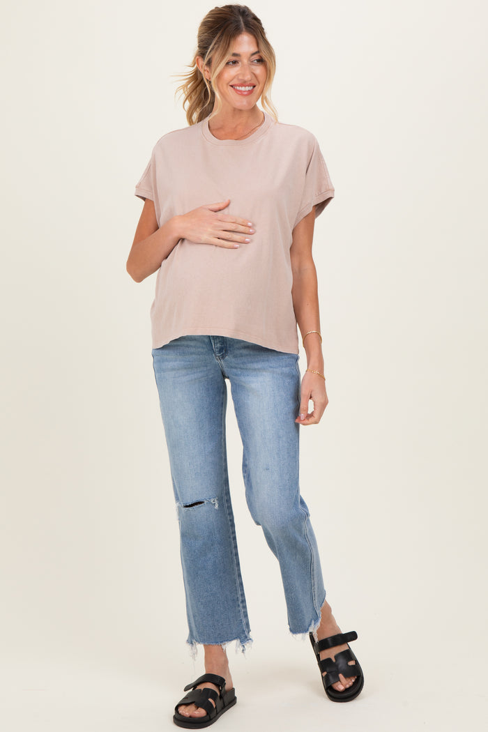 woman wearing a light pink maternity t-shirt and blue ripped jeans, holding her baby bump