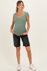 woman wearing a light green ribbed short sleeve maternity top and black denim shorts, showing her baby bump