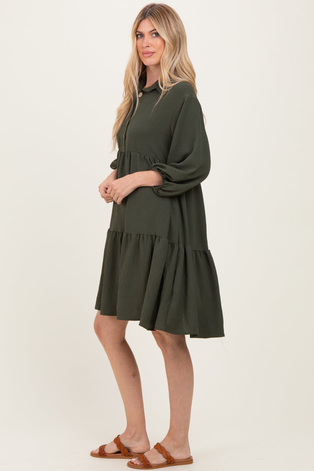 woman wearing a dark green tiered dress with puff sleeves and a collar, standing sideways