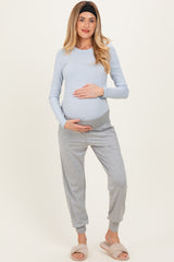 woman wearing a light blue long sleeve maternity top and gray jogger pants, gently cradling her baby bump