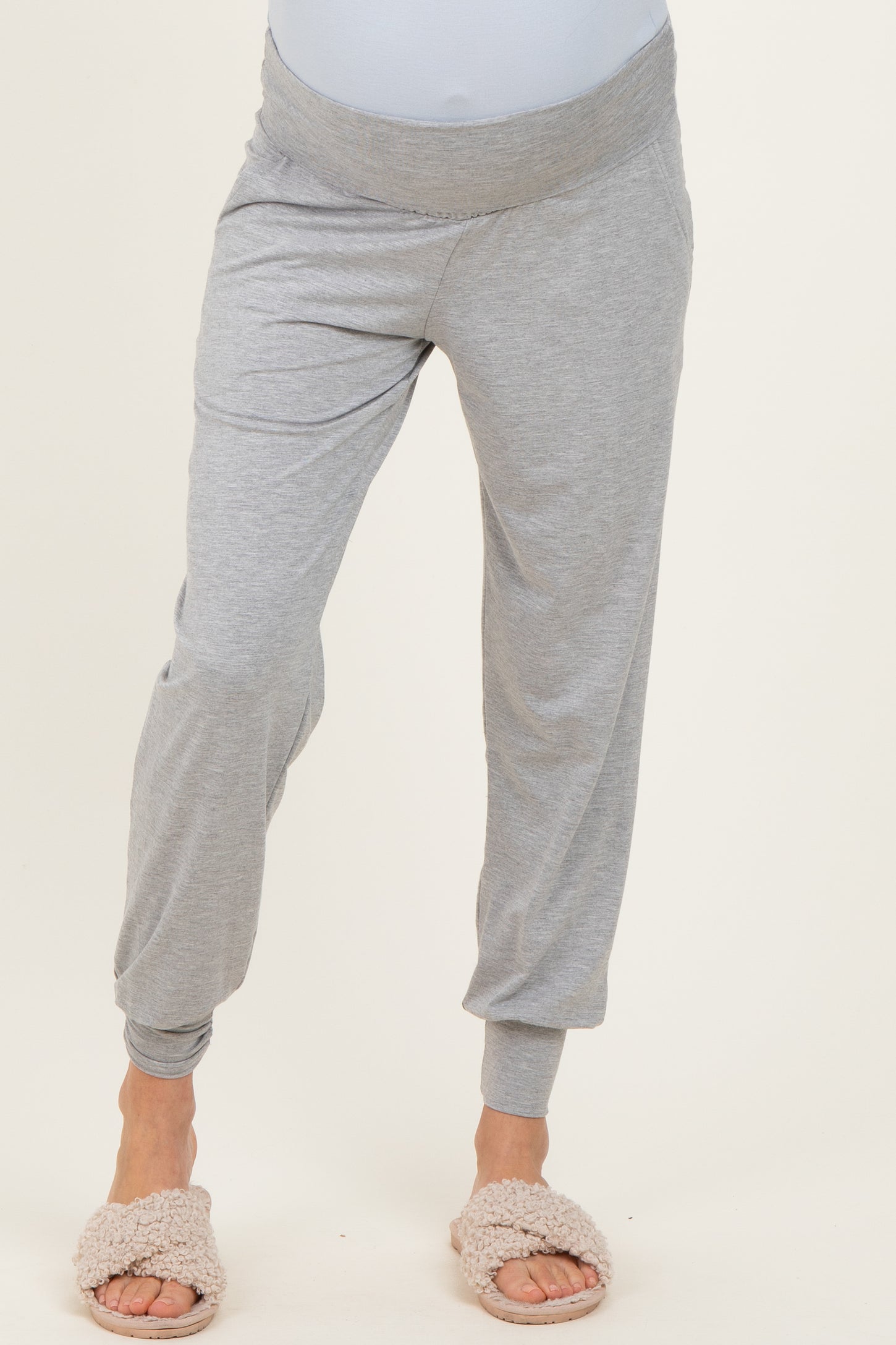 woman wearing light gray maternity jogger pants with a soft waistband and relaxed fit, styled with cozy slippers