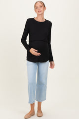 woman wearing a black ribbed long sleeve maternity top and light blue wide-leg jeans, holding her baby bump
