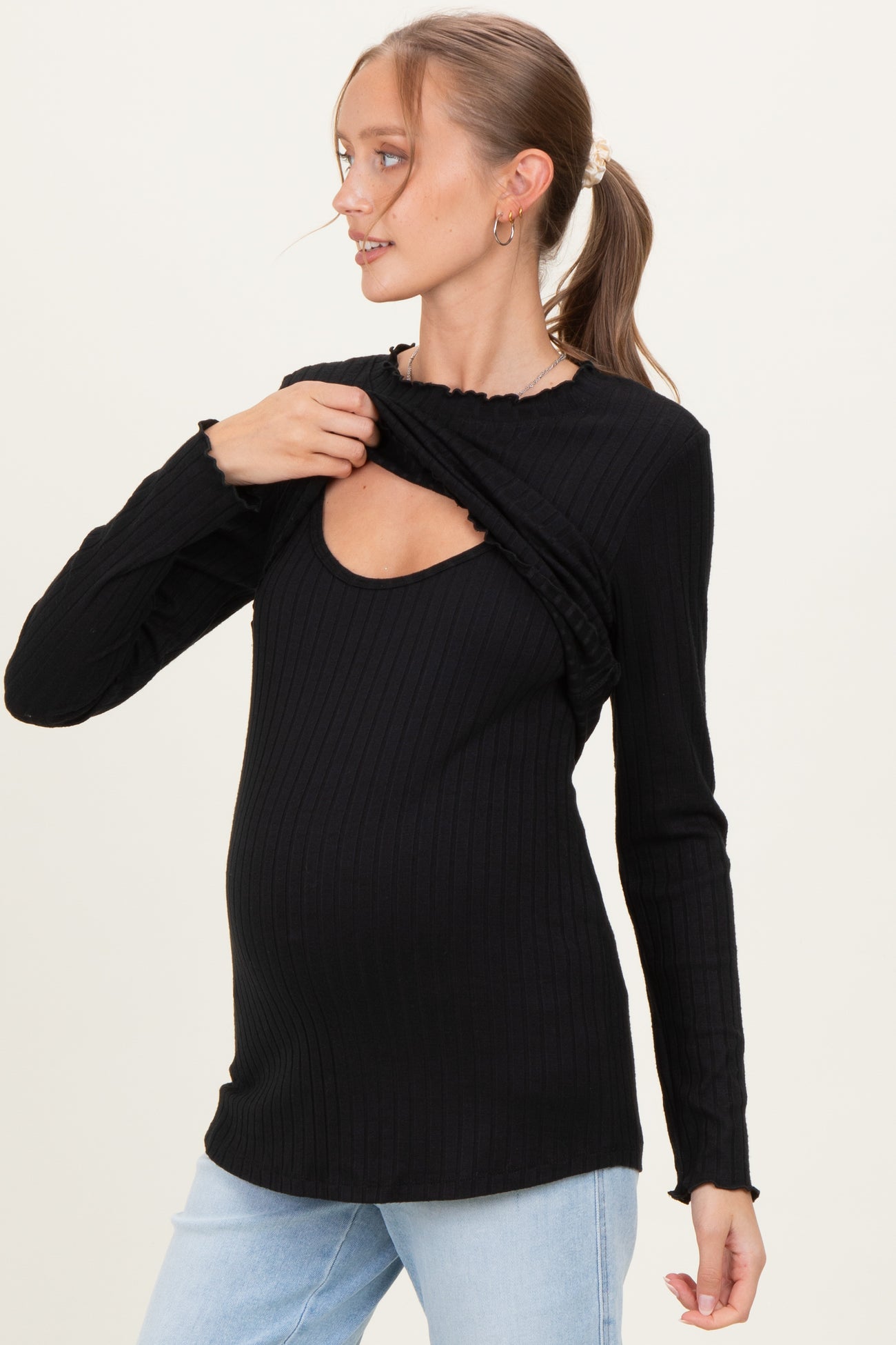 woman wearing a black long sleeve maternity top with a scoop neckline and ruffled detail, showcasing her baby bump