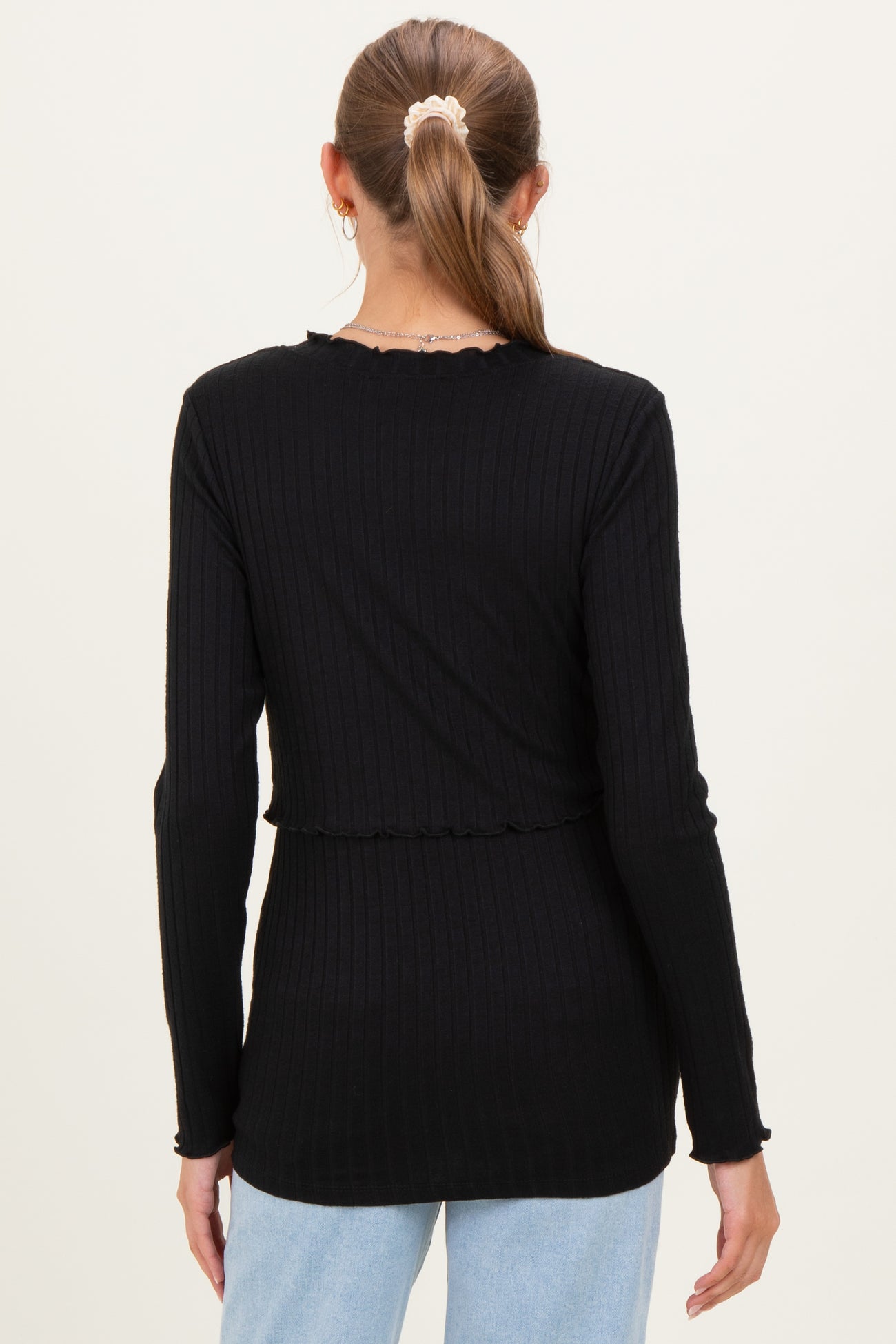 woman wearing a black long sleeve maternity top with ribbed texture and frill details, showing her back