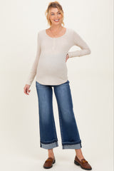 woman wearing a beige maternity long sleeve top and blue wide-leg jeans, showing her baby bump