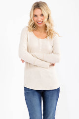 woman wearing a beige long sleeve henley top with button details and smiling, paired with blue jeans