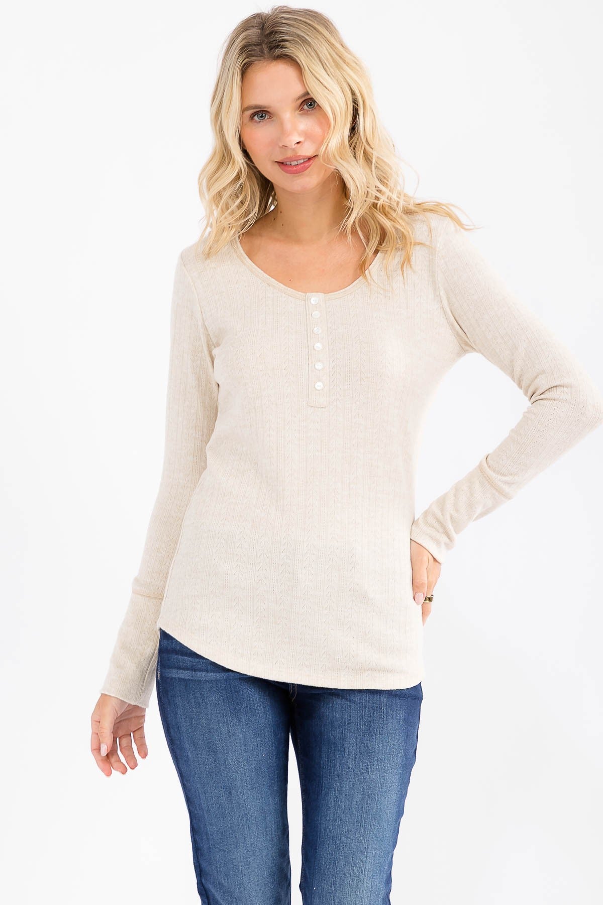 woman wearing a light beige long sleeve henley top with button details and a rounded hem, paired with blue jeans