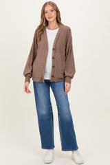 woman wearing a brown textured maternity cardigan over a white top paired with blue maternity jeans and white sneakers