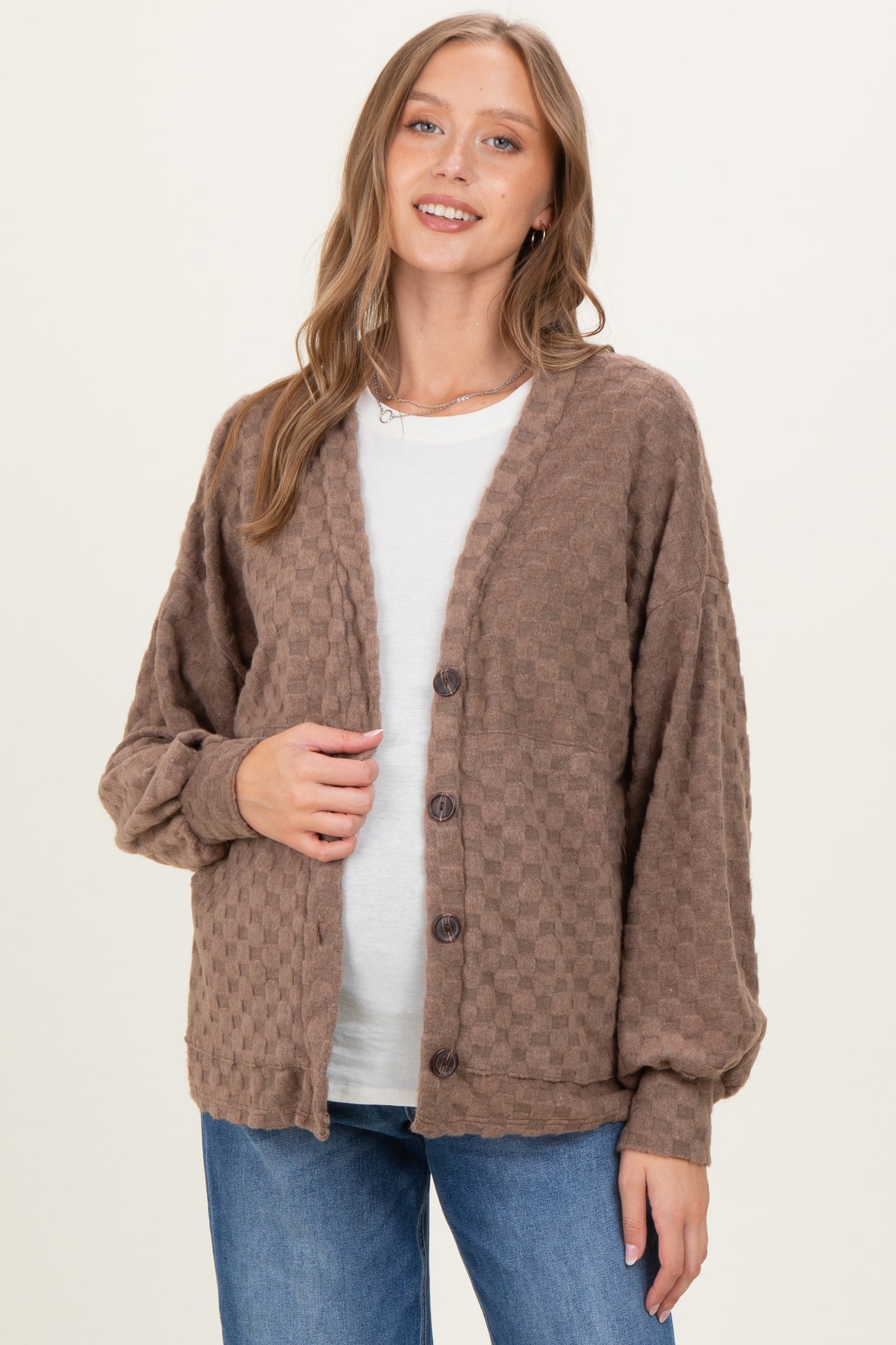 woman wearing a brown textured maternity cardigan over a white top and holding her baby bump