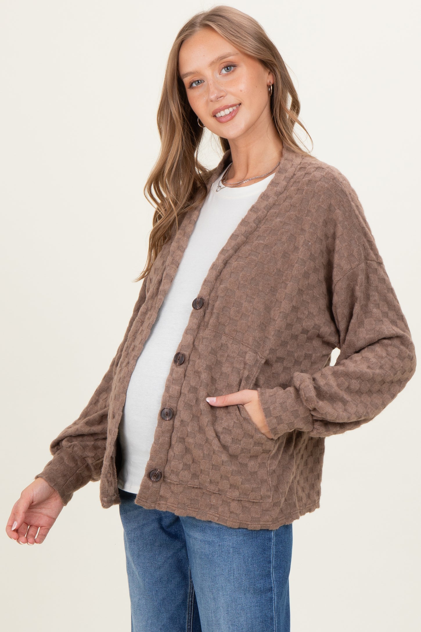 woman wearing a brown waffle knit maternity cardigan over a light gray top and showing her baby bump