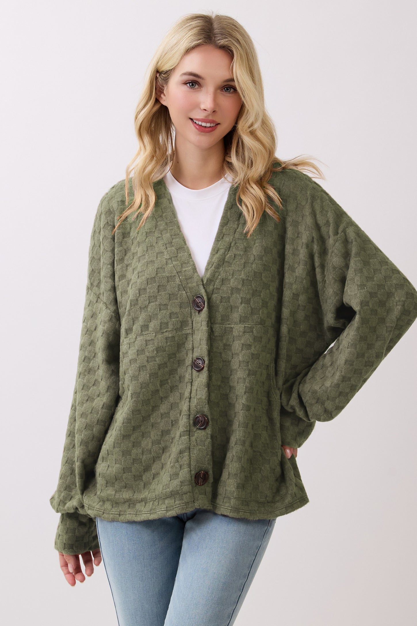 woman wearing an olive green textured button-up cardigan over a white shirt with light blue jeans