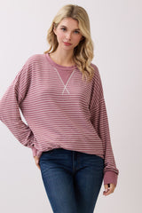 woman wearing a mauve striped long sleeve oversized sweatshirt with a v-neck and relaxed fit, paired with blue jeans