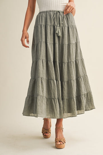 woman wearing a tiered olive green maxi skirt with a drawstring waist and tassel details