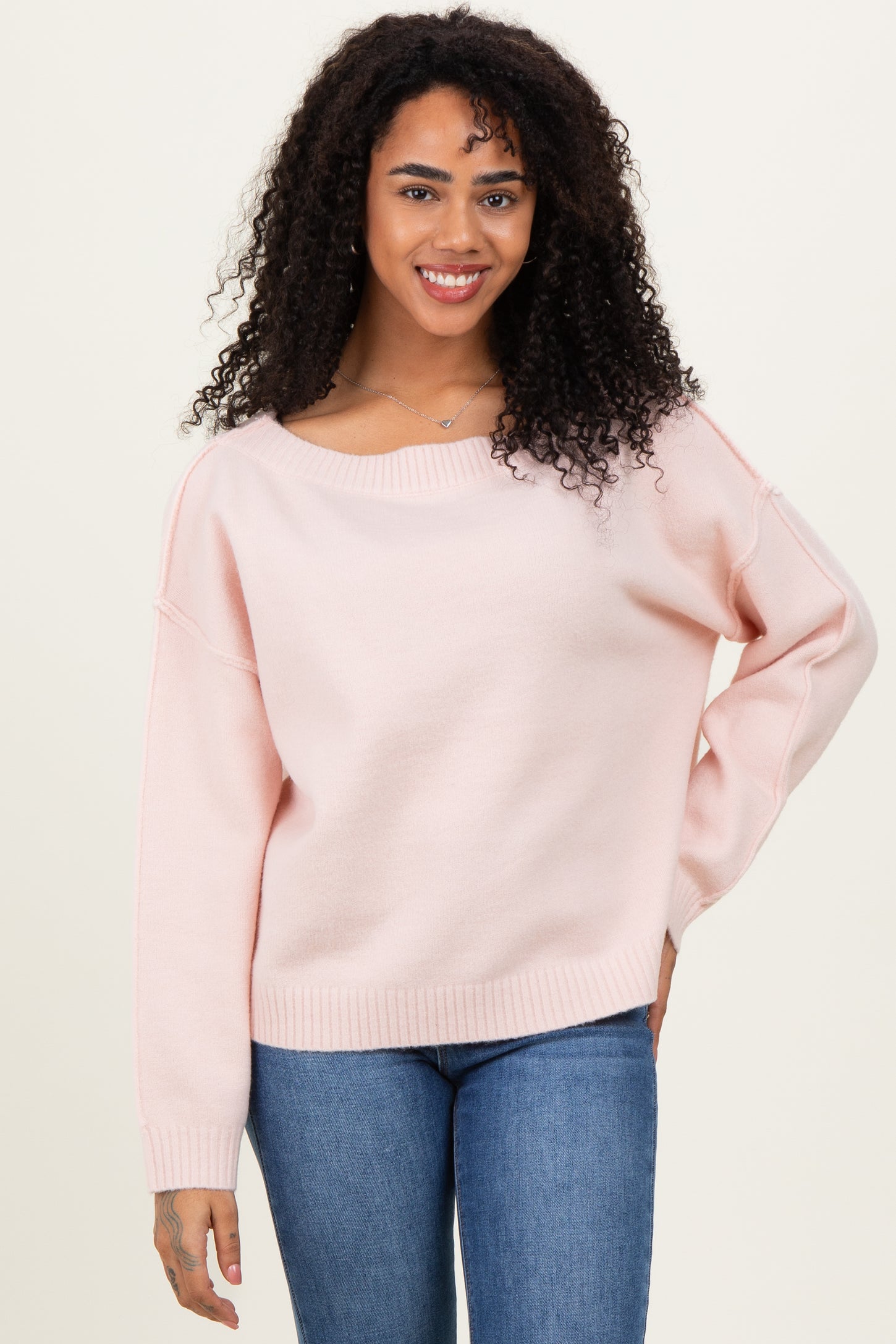 woman wearing a light pink oversized sweater with a wide neckline and long sleeves, paired with blue jeans