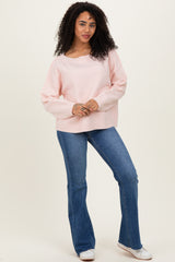 woman wearing a light pink oversized sweater and blue flared jeans, standing with one hand on her hip