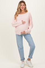 woman wearing a pink oversized maternity sweater and blue jeans, holding her baby bump