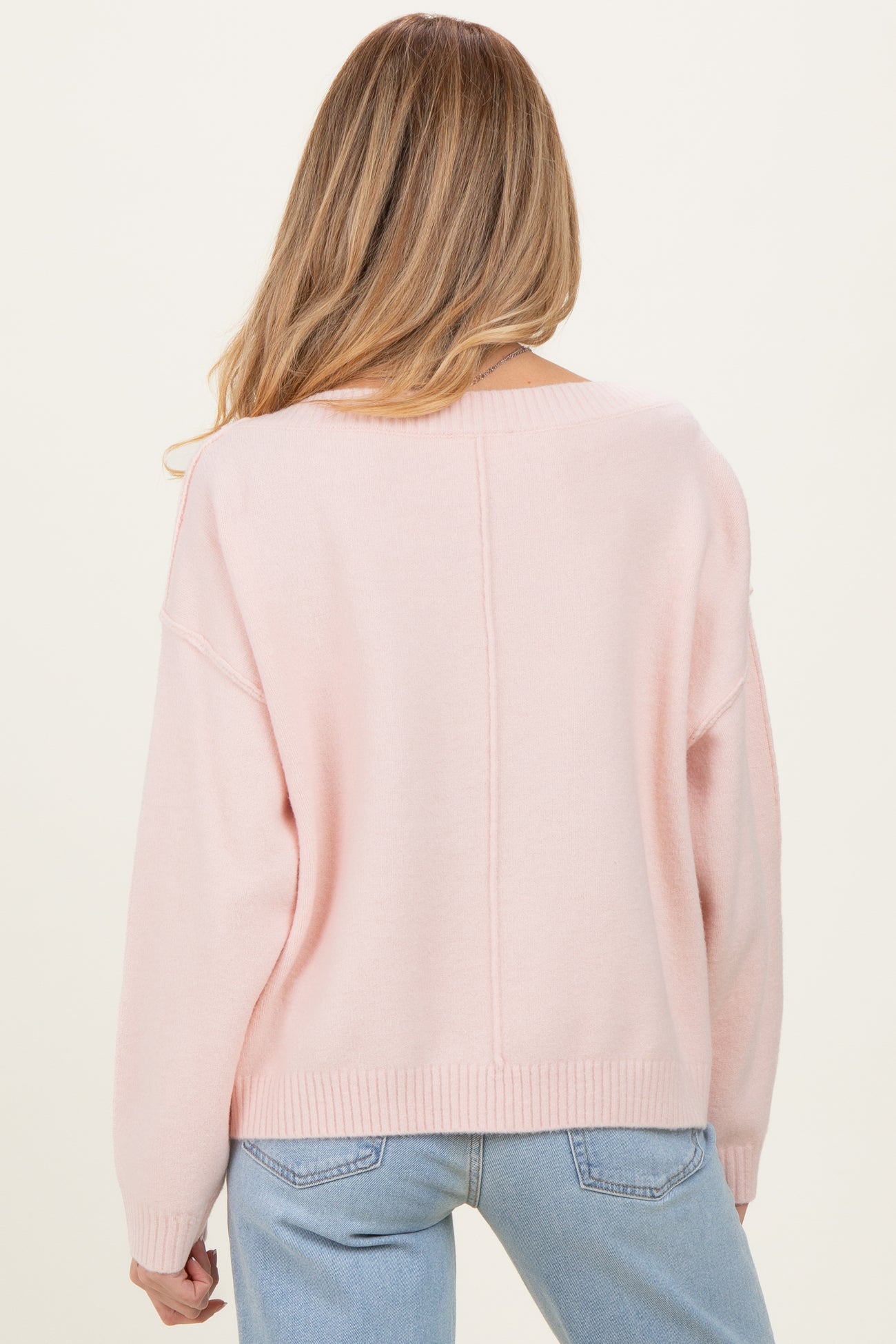 woman wearing a light pink maternity sweater with a loose fit and dropped shoulders, viewed from the back