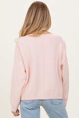 woman wearing a light pink maternity sweater with a loose fit and dropped shoulders, viewed from the back