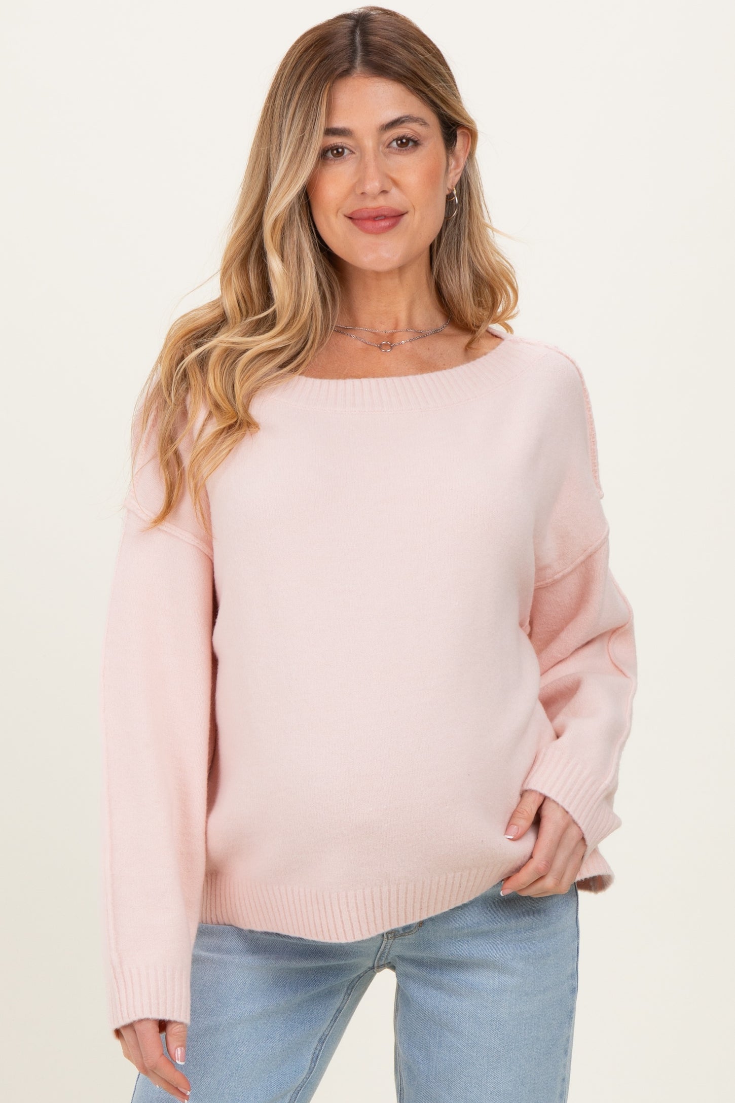 woman wearing a light pink oversized maternity sweater and showing her baby bump