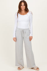 woman wearing a white long sleeve top and light gray wide-leg pants, standing with hands in pockets