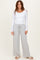 woman wearing a white long sleeve top and light gray wide-leg pants, standing with hands in pockets