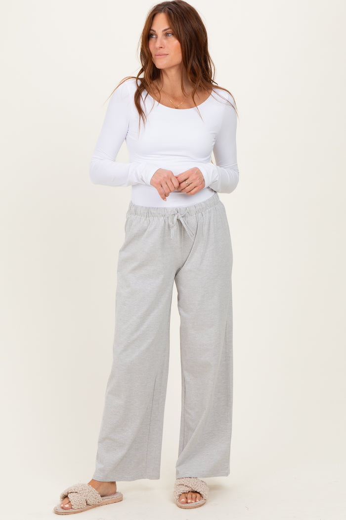 woman wearing a white long sleeve fitted top and light gray drawstring wide-leg pants, with cozy slippers