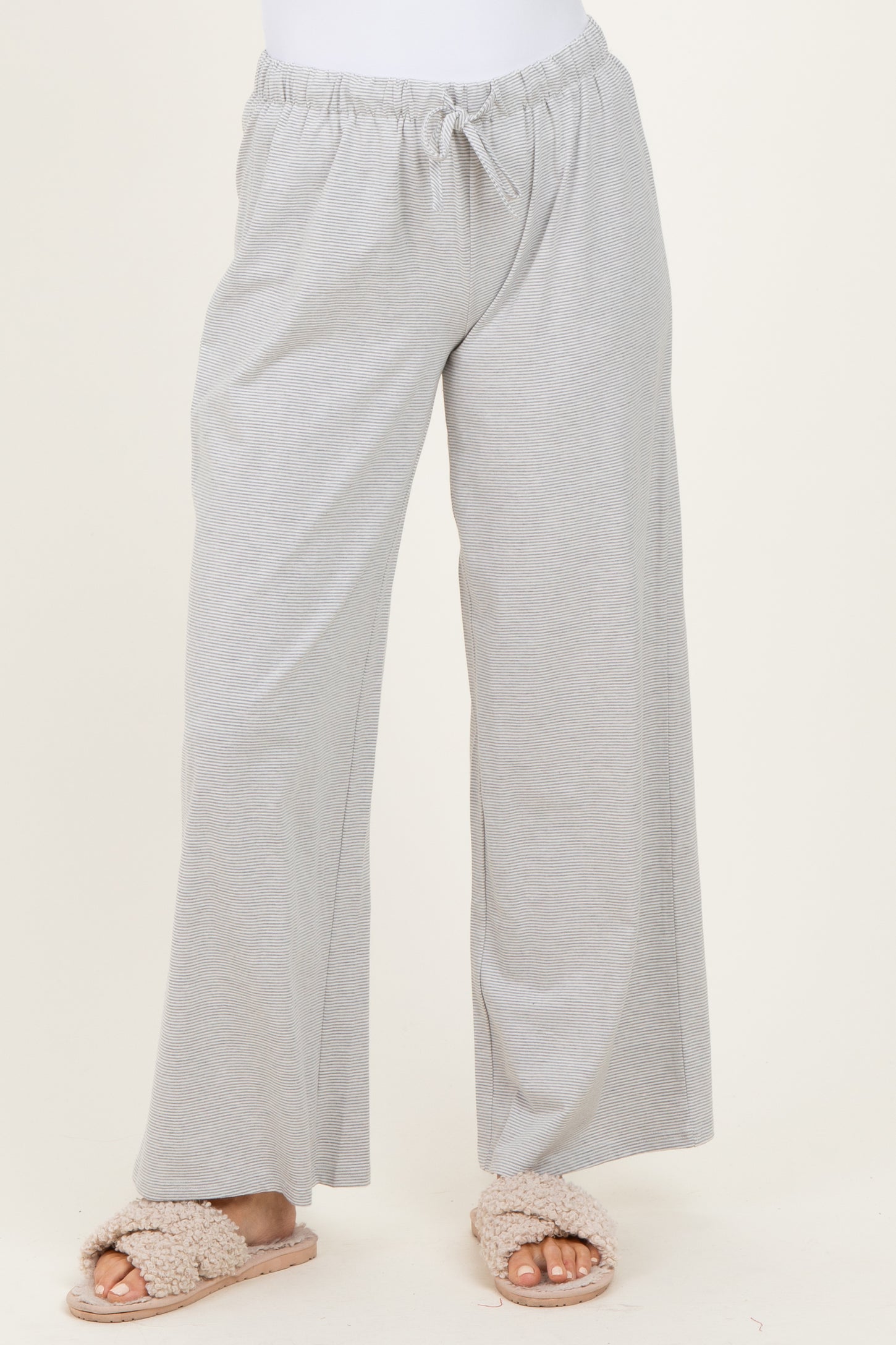 woman wearing light gray wide-leg lounge pants with an elastic waistband and drawstring detail, paired with fluffy slippers