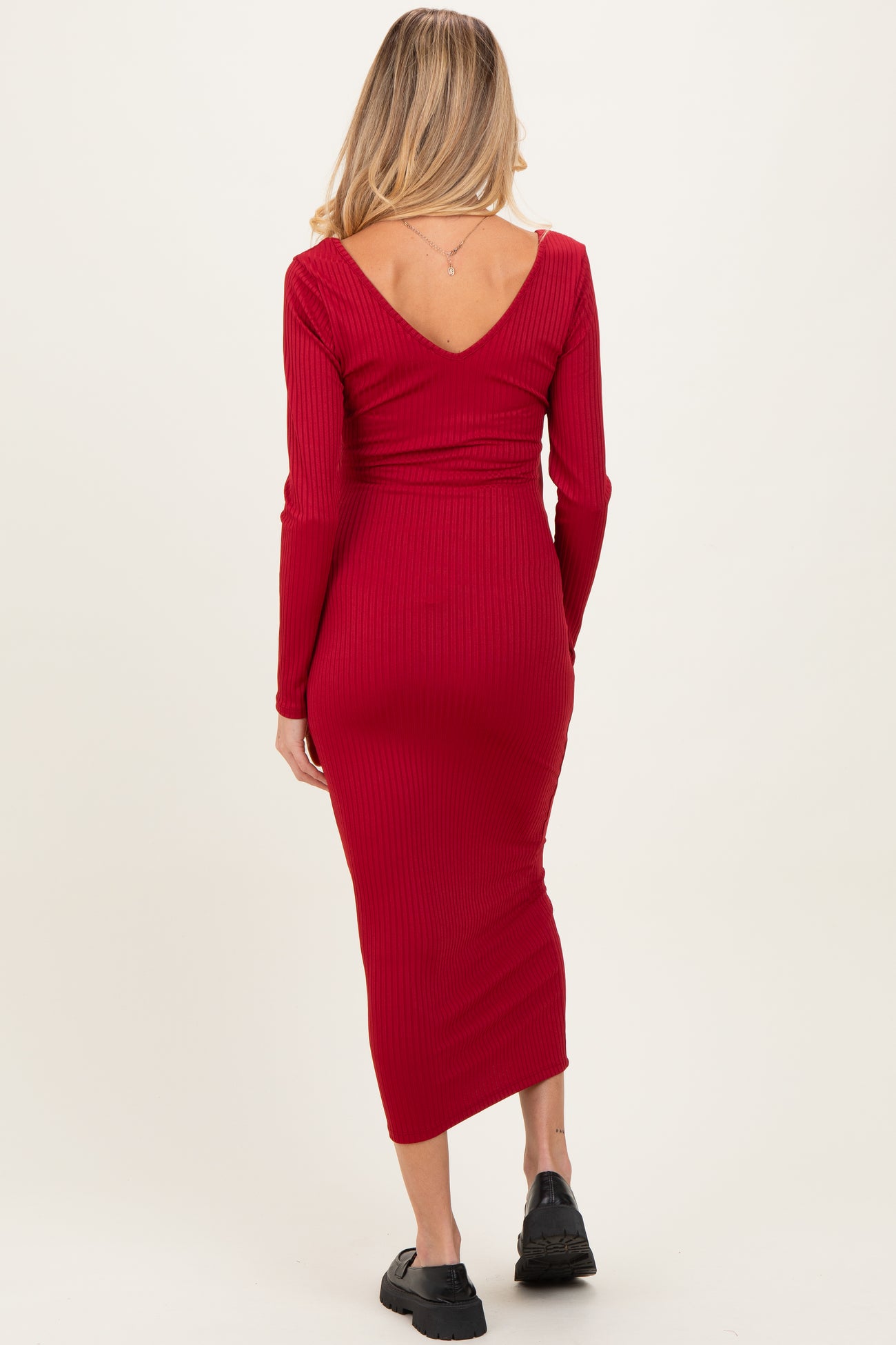 woman wearing a form-fitting red ribbed maternity dress with a V-back and long sleeves, showing for a baby bump