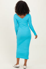 woman wearing a turquoise ribbed midi dress with long sleeves and a v-back detail, standing with her back to the camera