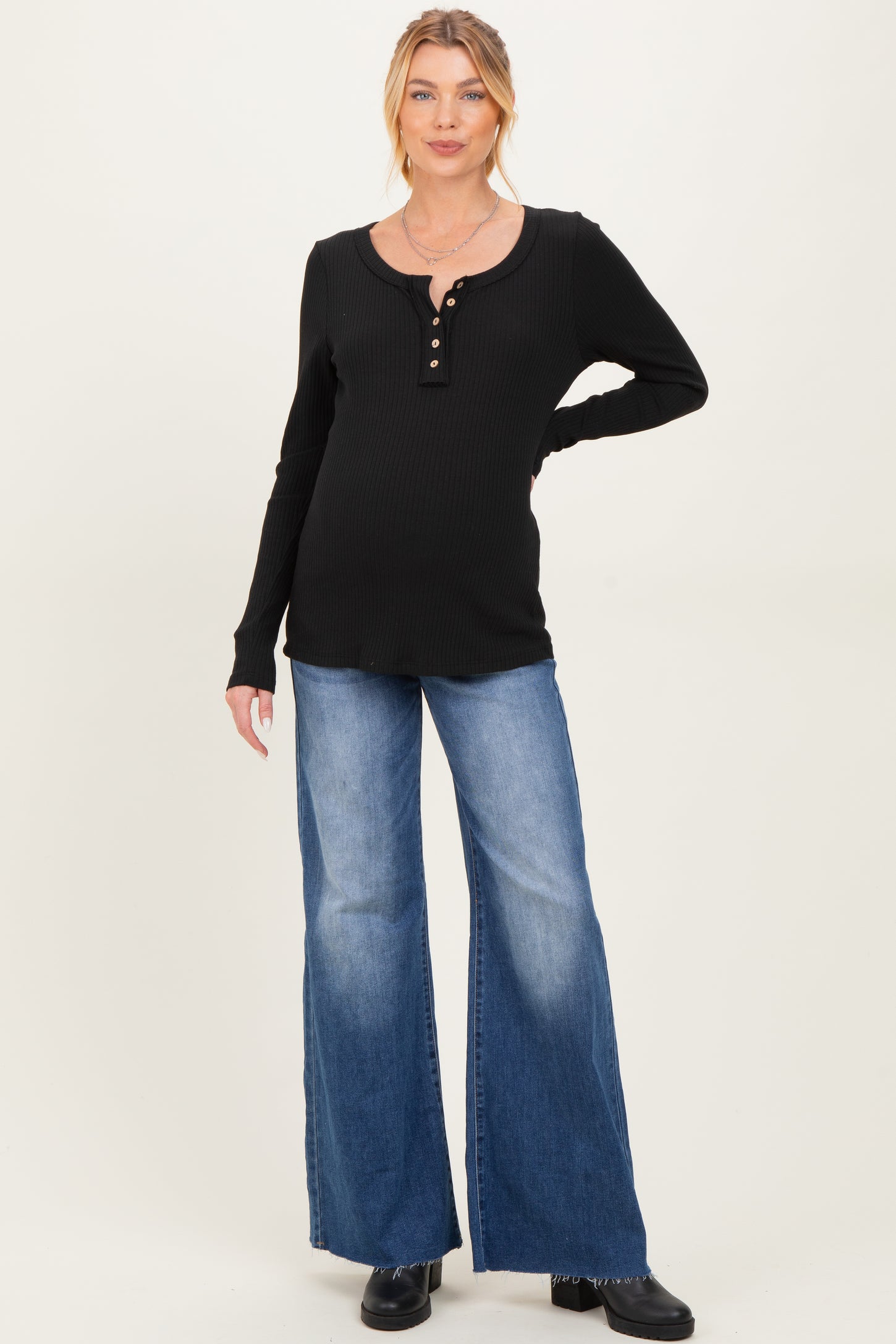 woman wearing a black ribbed maternity long sleeve henley top and blue wide-leg jeans, showing her baby bump